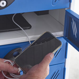 Hand placing a smartphone into a blue charging locker beside a tablet and cable